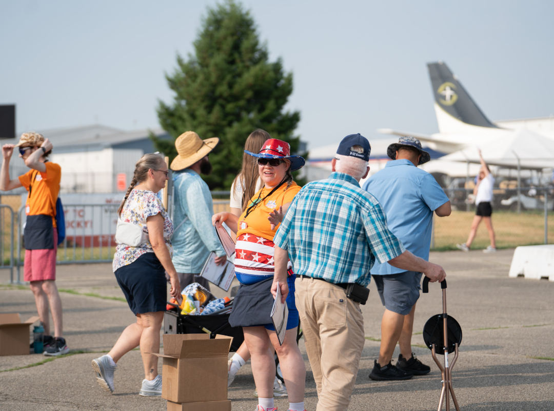 Volunteer Volunteers at the Dayton Air Show help guests and distribute materials near the flight line entrance. A smiling volunteer in a patriotic hat and shirt assists attendees, reflecting the welcoming spirit of the event’s volunteer team.