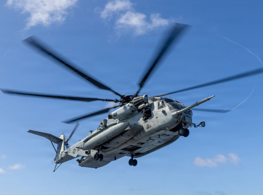 U.S. Marine Corps CH-53 heavy-lift helicopter flying with landing gear extended against a blue sky.