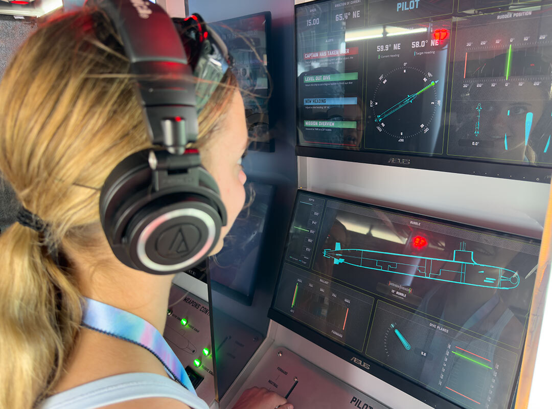 Young participant wearing headphones operates a hands-on aviation simulator with digital flight instruments and aircraft system displays during the Aviate Her experience at the CenterPoint Energy Dayton Air Show.