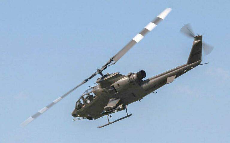 An AH-1F Cobra attack helicopter flying against a clear blue sky.