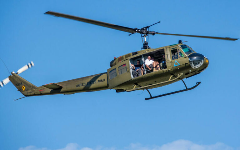 A UH-1 Huey helicopter in flight with passengers visible in the open side door, part of the ride experience at the Dayton Air Show.