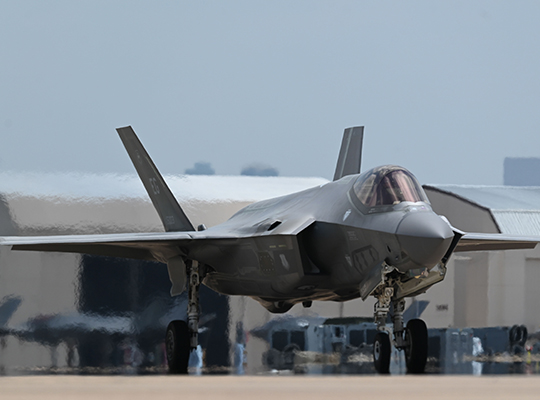 USAF F-35A Lightning II taxiing on runway with hangar structures behind