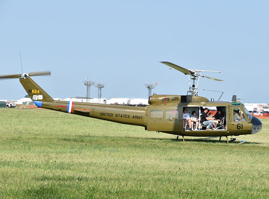 UH-1 Huey helicopter in flight over grassy field with passengers visible