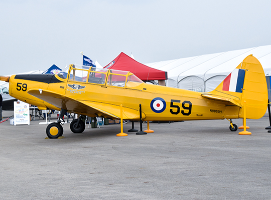 Yellow PT trainer aircraft on display with RAF roundels and event tents behind