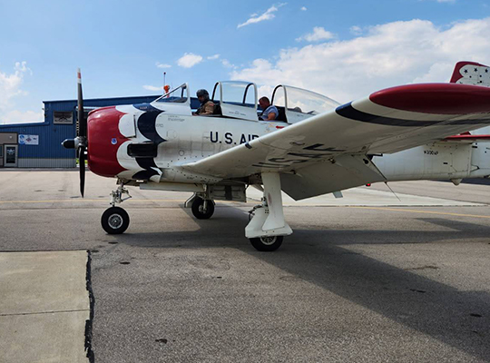 T-28 Trojan aircraft parked on ramp with red and white paint scheme and hangar in background