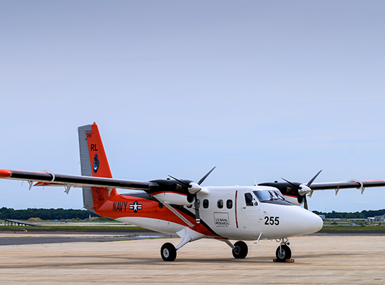 U.S. Navy Twin Otter aircraft parked on runway with orange markings