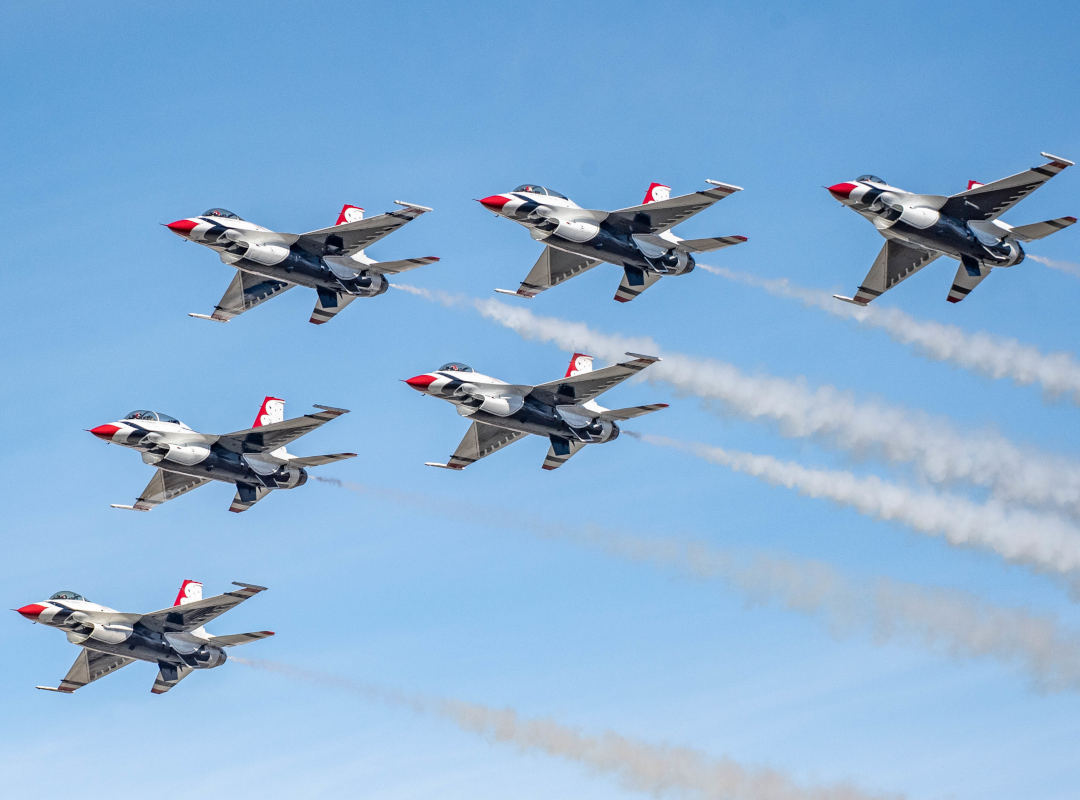Six U.S. Air Force Thunderbirds F-16 fighter jets flying in formation with smoke trails against a clear blue sky.